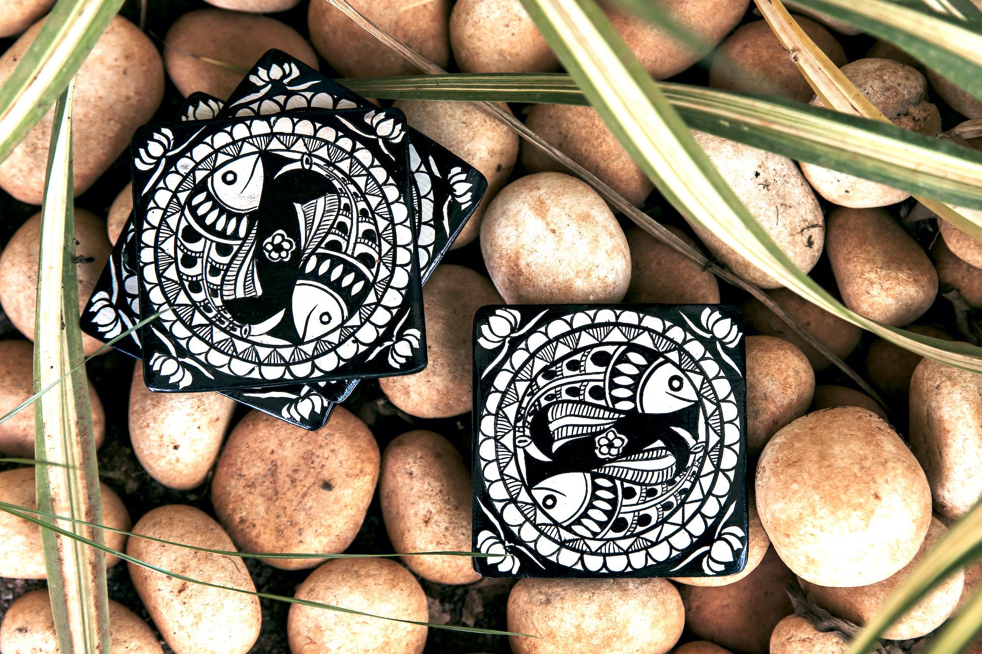A pair of black and white coasters with Pattachitra fish motifs on a bed of white pebbles