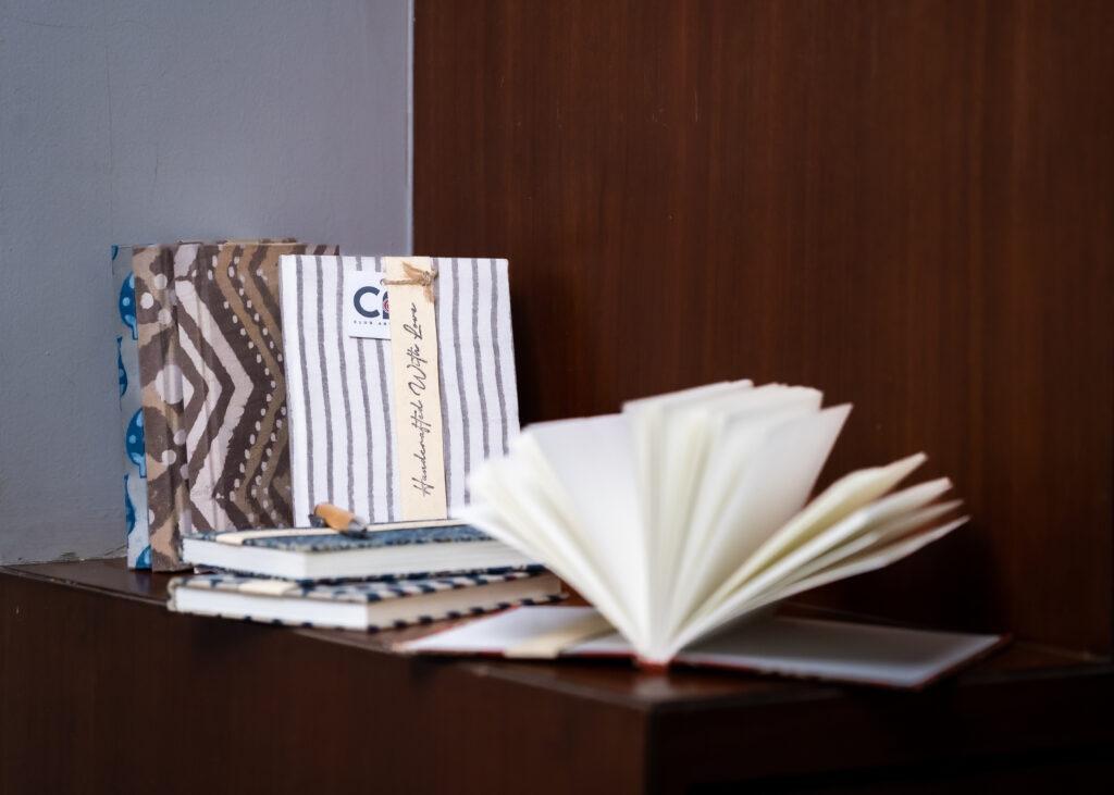 Image of several diaries on a desk. One of the diaries is open with handmade paper open like a fan. 