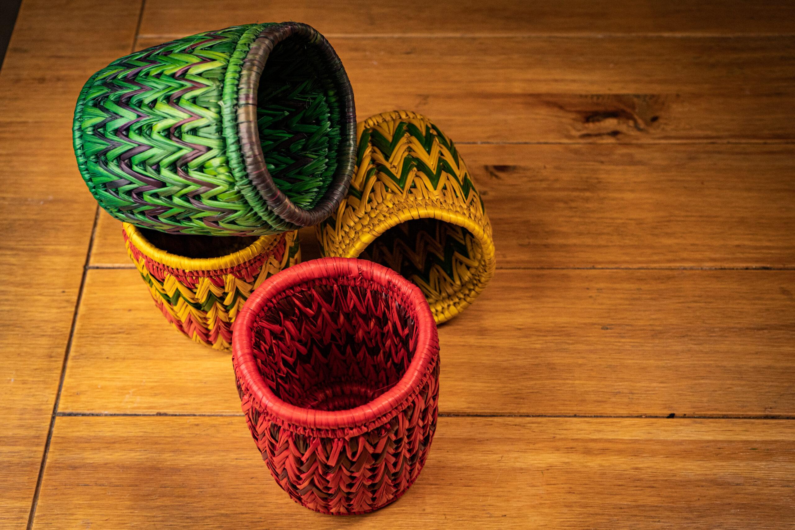Image of four pots made of Moonj grass in green red, yellow and multicolour on a brown wood surface