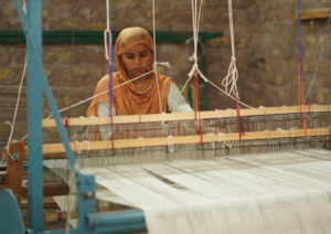 Image of a woman weaving. In the foreground is the loom