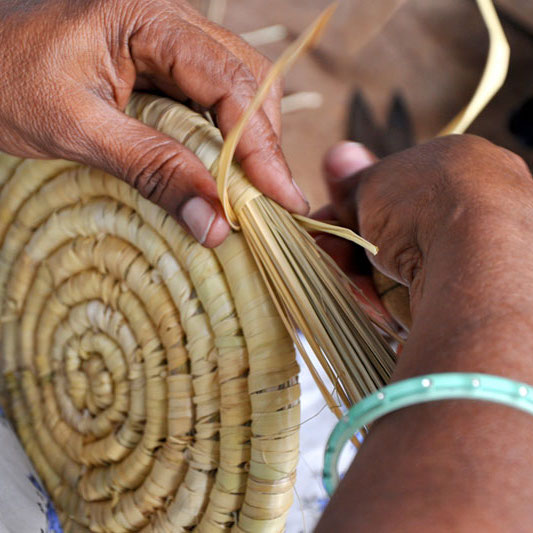 Close up of hands weaving together Moonj grass product. 